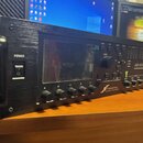 Černý rackový kytarový procesor s displejem a ovládacími prvky. Na předním panelu jsou nápisy POWER, FRACTAL AUDIO SYSTEMS a AXE-FX III. Zařízení má…