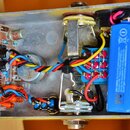 Interiér žlutého kovového šasi s nápisem Rooster na boku. Uvnitř se nachází elektronický obvod na desce s komponenty, modrá baterie s nápisy TESLA a…