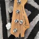 Hlava basové kytary z přírodního dřeva s čtyřmi chromovanými ladičkami. Na povrchu je čitelně uveden nápis Fender a PRECISION BASS®. Povrch dřeva vyp…