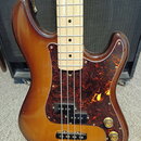 Čtyřstrunná elektrická basová kytara s tělem v hnědém sunburst provedení a javorovým hmatníkem. Nástroj má červeně vzorovaný pickguard, dva snímače a…
