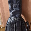 Černý polstrovatý pouzdro (gig bag) na hudební nástroj. Povrch je z černého syntetického materiálu s viditelným prachem a drobnými nečistotami. Zadní…