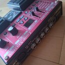 Červený looper s nápisy RC-30 DUAL TRACK LOOPER a LOOP STATION. Zařízení má několik tlačítek, dva posuvníky a dva otočné knoflíky. Na boční straně js…