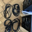 Na dřevěné podlaze leží dva černé reproduktory a tři černé napájecí kabely. Na zadní straně spodního reproduktoru je viditelné logo YAMAHA a nápisy M…