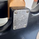 Detail zadní strany kytary v místě spoje krku s tělem. Černý lakovaný povrch vykazuje drobné oděrky na hraně u krku. Kovový kryt je připevněn čtyřmi…