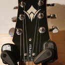 Černá hlava kytary s bílým logem Washburn v horní části a stylizovaným bílým symbolem uprostřed. Na spodní části hlavy je svisle napsaný bílý nápis W…