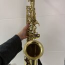 Zlatý saxofon v lakovaném provedení. Nástroj je držen rukou, na povrchu nejsou viditelné výraznější škrábance ani opotřebení. Na fotce nejsou žádná č…