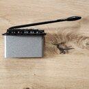 Fotografie zobrazuje kovový blok s černým tremolo mechanismem a páčkou. Blok je stříbrný s matným povrchem, mechanismus je černý. Na komponentu nejso…