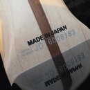 Detail zadní strany krku kytary z přírodního dřeva s tmavým pruhem uprostřed. Je zde černý nápis MADE IN JAPAN a pod ním modrým tiskem SERIAL NUMBER…