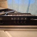 Zadní strana černého elektronického zařízení umístěného v hliníkovém přepravním kufru. Na zadním panelu jsou nápisy POWER, AC100-240V a čtyři výstupy…