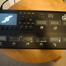 Černý kytarový procesor s displejem a ovládacími prvky. Na pravé straně je bílý nápis FRACTAL AUDIO SYSTEMS FM9 AMP MODELLER / FX PROCESSOR - MARK II…