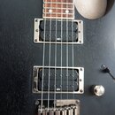 Černá elektrická kytara s hnědým hmatníkem. Nástroj má dva humbuckery, z nichž horní je označen nápisem INF3 a dolní nápisem INF4. V dolní části je v…