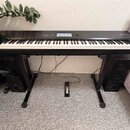 Černý digitální klavír s bílými a černými klávesami, umístěný na černém stojanu. Na pravé straně horního panelu je nápis NANTILUS. Instrument je dopl…