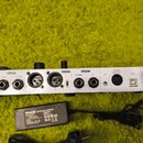 Zadní strana bílého elektronického zařízení s řadou konektorů a přepínačem. Jsou zde nápisy AUX IN, EXP 2, IN, FXLOOP (SEND, RETURN), XLR OUT, OUTPUT…