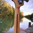 Zadní strana krku a hlavy basové kytary z přírodního dřeva s lakovaným povrchem. Na hlavě jsou vidět dva chromované ladičky a logo Fender. Podél krku…