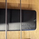 Detailní záběr na černý magnetický snímač s nápisem bartolini mk 1. Snímač je připevněn k dřevěnému tělu nástroje a přes něj vedou dvě kovové struny.…