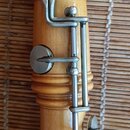 Detail dřevěného dechového nástroje světlé hnědé barvy s kovovým mechanismem klapek. Kovové části jsou stříbrné barvy a vykazují mírné známky opotřeb…