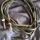 Černý audio kabel s dvěma 6,3mm jack konektory na jedné straně a jedním menším jack konektorem na druhé straně. Na jednom z velkých konektorů je vidě…