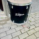Černý buben s kovovými obručmi a stojanem. Na korpusu je bílý nápis Zildjian. Povrch bubnu vykazuje drobné škrábance a opotřebení.