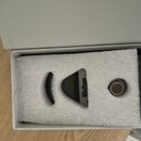 V bílé krabičce s pěnovou výplní je umístěn malý elektronický přístroj šedé barvy. Na přístroji je svisle napsaný nápis Minitune. Vedle něj se v otvo…