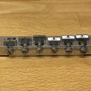 Kovový kobylkový mechanismus stříbrné barvy s šesti ladicími šrouby. Povrch vykazuje známky opotřebení a místní znečištění v drážkách pro struny. Na…