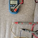 Na fotografii je digitální klepové měřidlo značky CEM s displejem ukazujícím hodnotu 6.93 a připojený k němu snímač kytary. Snímač je kovový, v béžov…