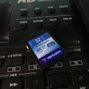 Na černém povrchu elektronického zařízení leží modrá SD karta značky verbatim. Na kartě je uveden nápis 32 GB Go, Premium a rychlost up to 90 MB/s. V…
