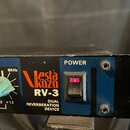 Detailní záběr na přední panel černého rackového zařízení. Je zde vidět modrý panel s nápisy POWER, Vesta Koza RV-3 a DUAL REVERBERATION DEVICE, dále…
