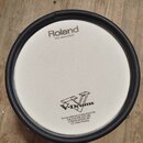 Bílá elektronická bubnová plocha s černým obvodovým rámem. Na povrchu je nápis Roland a pod ním text Head made by REMO, ve spodní části logo V-Drums.…