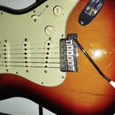 Elektrická kytara s tělem v provedení sunburst a krémovým pickguardem. Na knoflících jsou nápisy TONE a VOLUME. Nástroj má tři snímače, chromovaný mo…