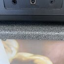 Detail zadní strany černého hudebního zařízení s třemi konektory. Jsou zde viditelné nápisy SUSTAIN, USB TO HOST a AUX IN. Povrch je matně černý s mí…
