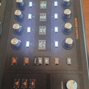 Černý syntezátor s ovládacími prvky a displeji. Na panelu jsou viditelné nápisy MAIN SYSTEMS, MASTER CONTROL, CUTOFF a RESONANCE. V dolní části jsou…