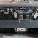 Zadní strana kytarového komba v černém texturovaném provedení. Na zadním panelu je nápis SUPER-SONIC 22 a pod ním FENDER MUSICAL INSTRUMENTS CORP. V…