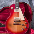 Elektrická kytara s tónem cherry sunburst v hnědo-červené barvě, umístěná v otevřeném hnědém kufru s červeným vnitřkem. Nástroj má dva humbuckery, kr…