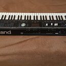 Černý digitální klavír s bílými a černými klávesami. Na přední straně je bílý nápis Roland a označení modelu VR-09. Ovládací panel obsahuje různé tla…