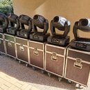 Šest kusů černých moving head světel umístěných na šesti odpovídajících transportních kufrech s kovovými hranami a kolečky. Na základnách světel jsou…