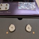 Sada In-ear monitorů v barvě stříbrné a černé, umístěná v černém boxu. Na obou sluchátkách je viditelné logo ve tvaru stylizovaného písmena „f“. V ho…