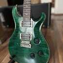 Elektrická kytara s tmavě zeleným lakem a výraznou strukturou dřeva. Nástroj má dva humbuckery, tři ovládací knoflíky a strunoměr. Na hrazdici jsou v…