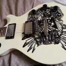 Bílá elektrická kytara s černým grafickým motivem na těle, který obsahuje nápis Anarchy. Nástroj má dva humbuckery s chromovanými kryty, čtyři černé…