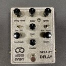 Stříbrný efektový pedál s nápisy AUDIO EVENT a DREAMY DELAY. Zařízení má šest černých otočných knoflíků s popisky delay time, delay, speed, feedback,…