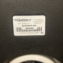Detailní záběr na bílou nálepku s černým textem nalepenou na tmavém, strukturovaném povrchu. Na nálepce je logo Quilter s nápisem Amplification, adre…