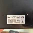 Černý přístroj s bílou nálepkou. Na nálepce je text DMX 6Fire USB, Made in Taiwan a značka CE. Je zde uveden kód 20048717131946800466, čárcový kód a…
