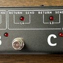 Detailní záběr na ovládací panel šedého elektronického zařízení. V horní části jsou bílé nápisy RETURN a SEND rozdělené do sekcí LOOP1 a LOOP2, dopln…