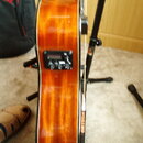 Detail akustické kytary s lakovaným povrchem v žlutohnaté barvě. Na boku korpusu je umístěn černý ovládací panel s knoflíky a displejem. Vedle kytary…