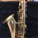 Zlatý saxofon s lesklým povrchem, umístěný v černém pouzdře. Nástroj má standardní tvar s viditelným zvukovodem a mechanismem klapek. Na fotce nejsou…