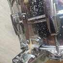Detail chromovaného mechanismu na straně bubnu. Na kovovém raménku je svisle napsán nápis "Ludwig". Povrch bubnu vykazuje výrazné opotřebení, jsou na…