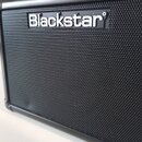 Detailní záběr na přední stranu černého kytarového komba s kovovou mřížkou. V horní části je umístěno bílé logo Blackstar. Povrch mřížky i rámu vypad…