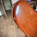 Detailní záběr na hranu a povrch hřidnu kytary v hnědé barvě s viditelnou strukturou dřeva. Lakovaný povrch vykazuje známky opotřebení ve formě drobn…