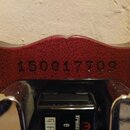 Detail zadní strany hlavy kytary z červeného dřeva s viditelnou strukturou slátek. Uprostřed je vyrazeno sériové číslo 150017709. Ve spodní části jso…
