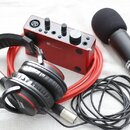 Sada červeného a černého audio vybavení na světlém podkladu. Obsahuje červený zvukový interface s nápisem Focusrite, černý mikrofon s popsem a nápise…