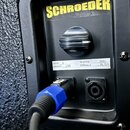 Detail zadní strany černého reproduktorového boxu se značkou SCHROEDER v žlutém obdélníku. Na bílém štítku jsou uvedeny údaje OHM: 8, WATTS: 600, MOD…
